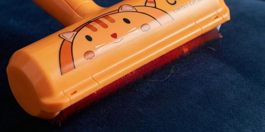 A close-up view of the orange 'ChomChom Home Limited Cat Edition' pet hair roller resting on dark blue velvet fabric. The red bristle pad is visible underneath, holding some trapped pet hair.